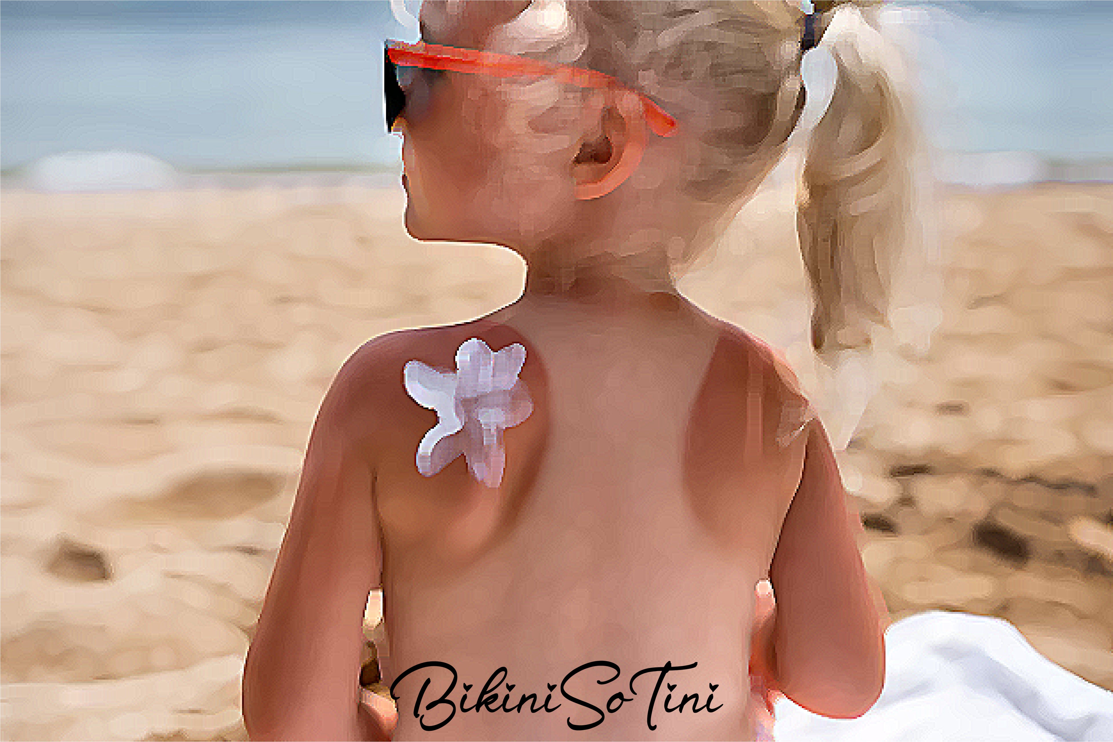 Child on a beach with a flower-shaped sun screen on their shoulder, wearing sunglasses.