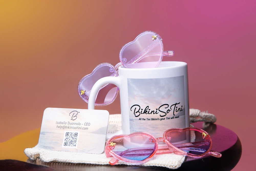 Mug with 'Bikini So Tini' branding, heart-shaped sunglasses, and business card on a gradient background