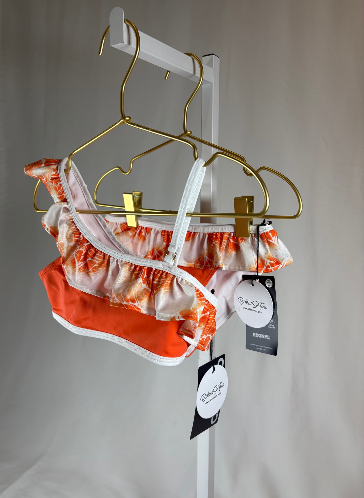 Orange and white patterned bikini set on a gold hanger against a plain background