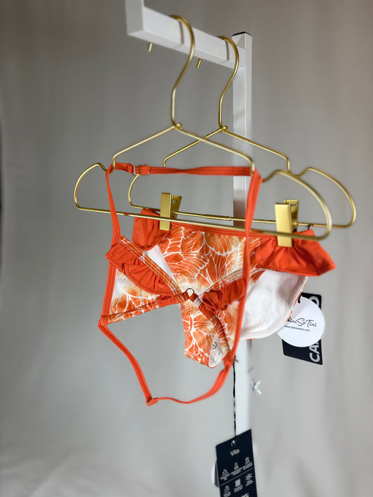 Orange and white patterned lingerie set on a gold hanger against a gray background