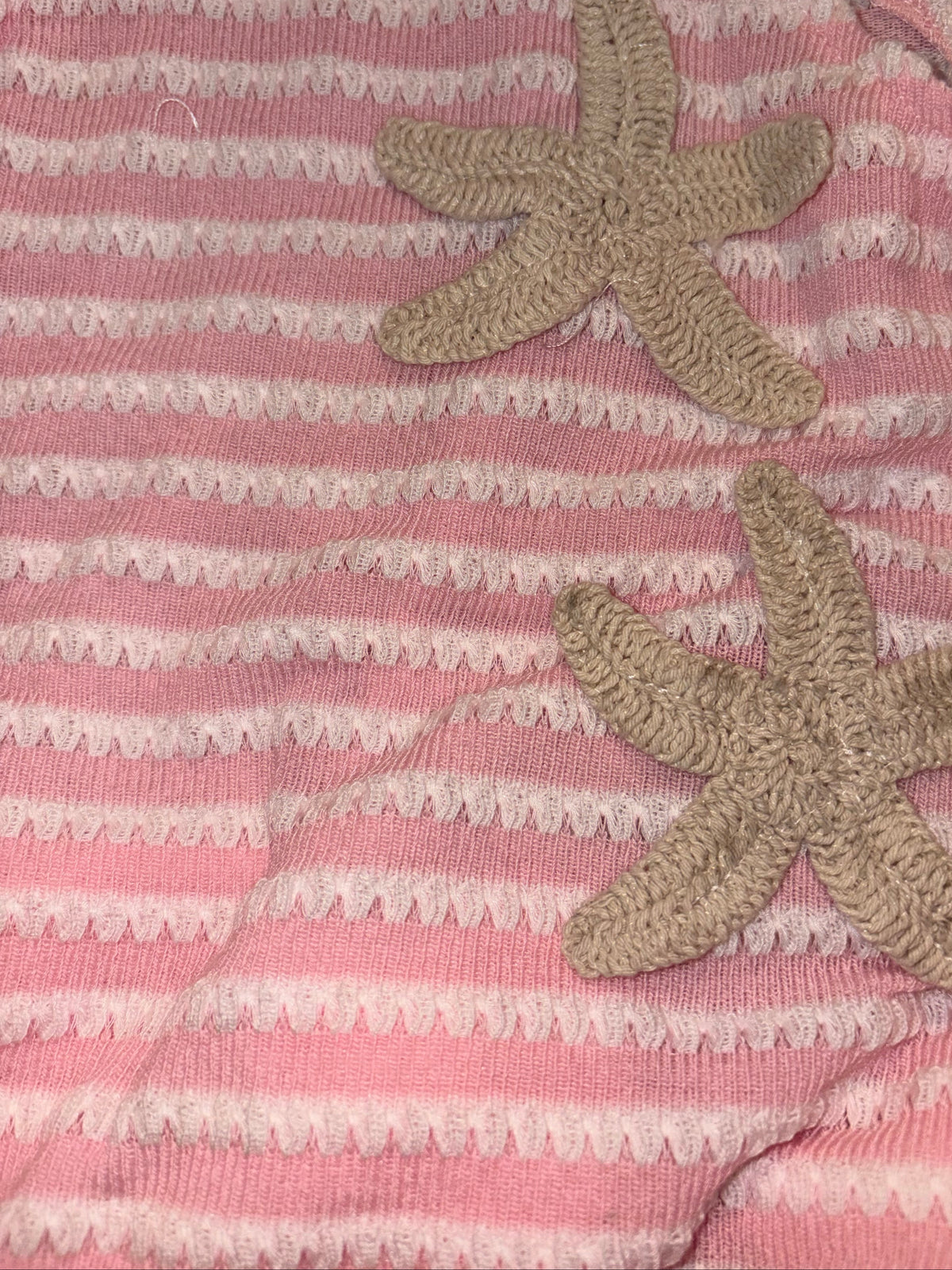A close-up of a pink and white striped knit fabric with two beige starfish appliqués on the front.